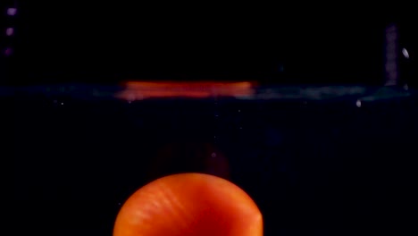 high speed camera slow motion reverse video of a red tomato splashing into the water with black background