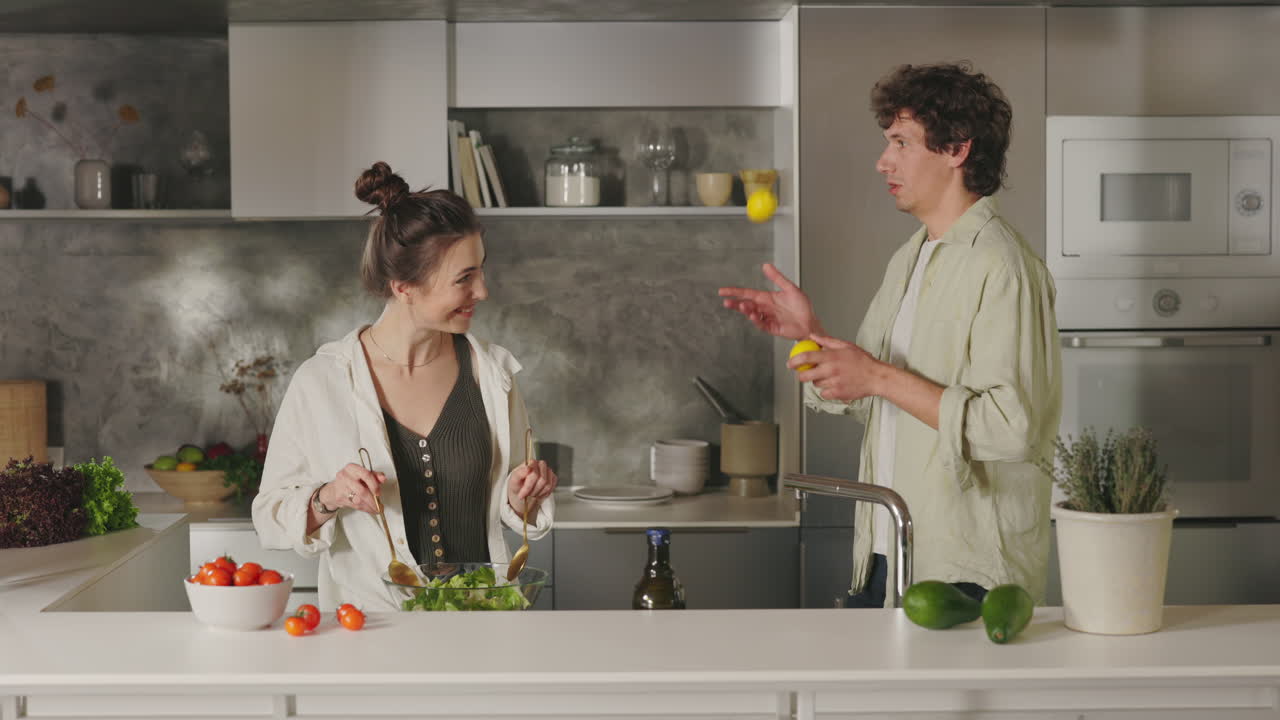 Coppia che si gode il tempo in una cucina moderna, preparando cibo e facendo giocoleria con i limoni