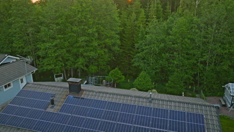 Solar-house-in-middle-of-dense-forest,-summer-sunrise---Ascending-aerial-shot