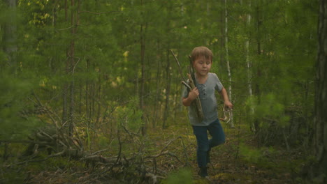 boy 3 carries sticks in woods that will be used to light a camper camper