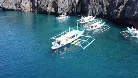 traditional outrigger island hopping tour boats anchored at the secret beach, el nido philippines