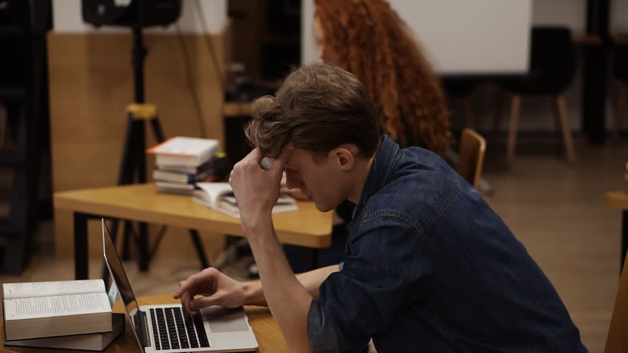 도서관에서 노트북을 사용하는 집중된 젊은 남자의  ⁇ 보기. 공공 또는 대학 도서관에서 공부하는 예쁜 유럽 학생. 교육 개념