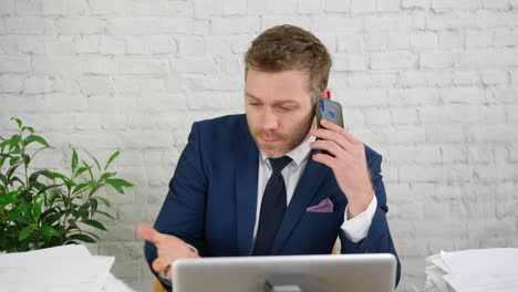 an overworked businessman in an office is stressed and frantic with his busy workload and is under preassure whilst talking on the phone