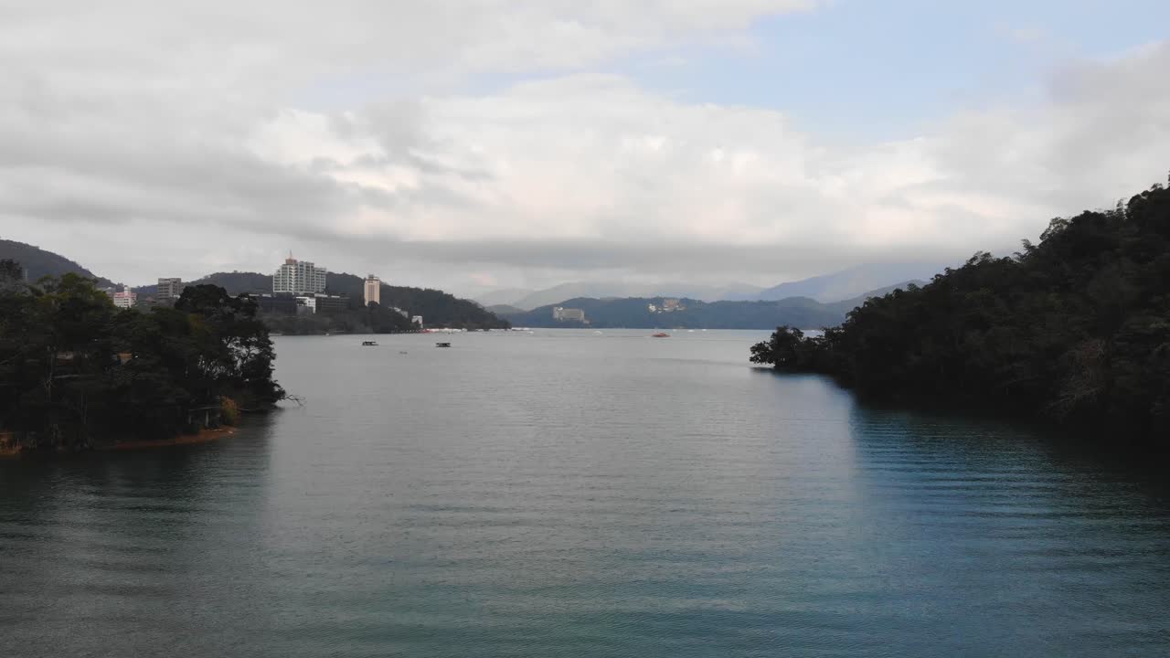 Sun Moon Lake in 4K drone aerial shot, fly over the surrounding forest trees and lake water with a view of boats and buildings, Yuchi Township, Nantou County, Taiwan.