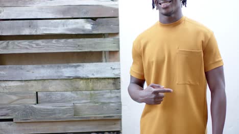 feliz hombre afroamericano con camiseta amarilla apuntando al bolsillo, cámara lenta, espacio de copia