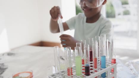 African-american-boy-sitting-at-table-holding-test-tubes-with-liquid,-in-slow-motion