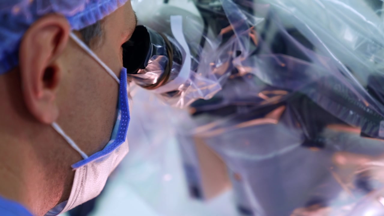 Uomo caucasico con mascherina e cuffia che guarda i binocoli del microscopio. Ritratto del chirurgo che esegue l'operazione. Primo piano.