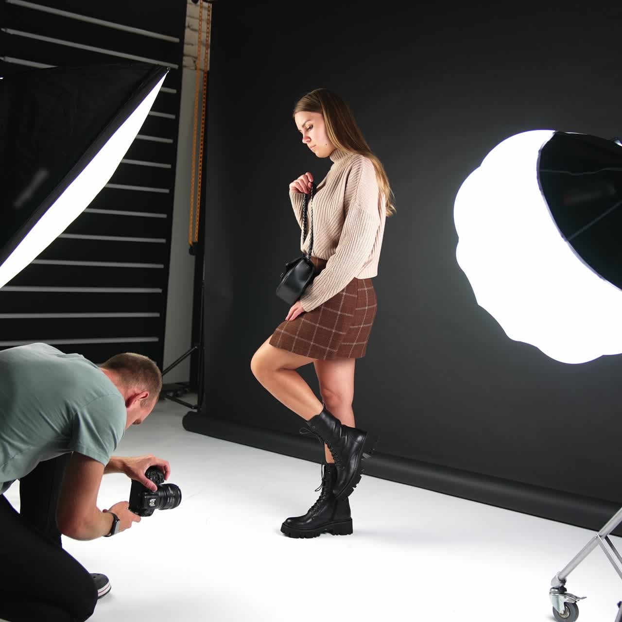 Girl posing in front of camera demonstrating fashionable footwear and bag. Backstage of a photographer working in the studio