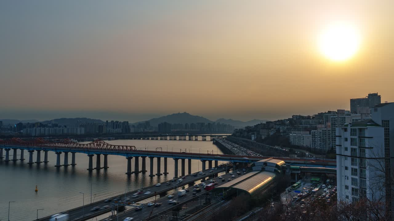 Seul, Corea del Sud - hyperlapse con zoom indietro, traffico sull'autostrada Gangbyeonbuk-ro, Ponte Donho, Stazione Oksu stagliata contro un vivido tramonto dorato, riflessi del fiume Han, montagne, foschia invernale