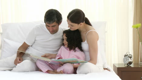 Padres-Leyendo-Un-Libro-En-La-Cama-Con-Su-Hija-