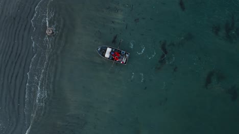 birdseye view of fisherman rowing boat met by friend helping pull boat ashore