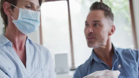 Caucasian-female-dental-nurse-with-face-mask-examining-teeth-male-patient-at-modern-dental-clinic