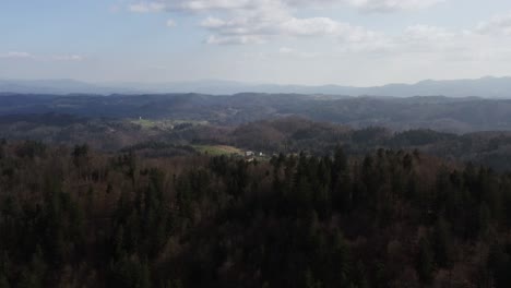 Neblige-Waldlandschaft,-Die-Sich-Bis-In-Sanfte,-Dunstige-Berge-Erstreckt,-Unterbrochen-Von-Offenen-Feldern-Und-Abgelegenen-Gehöften