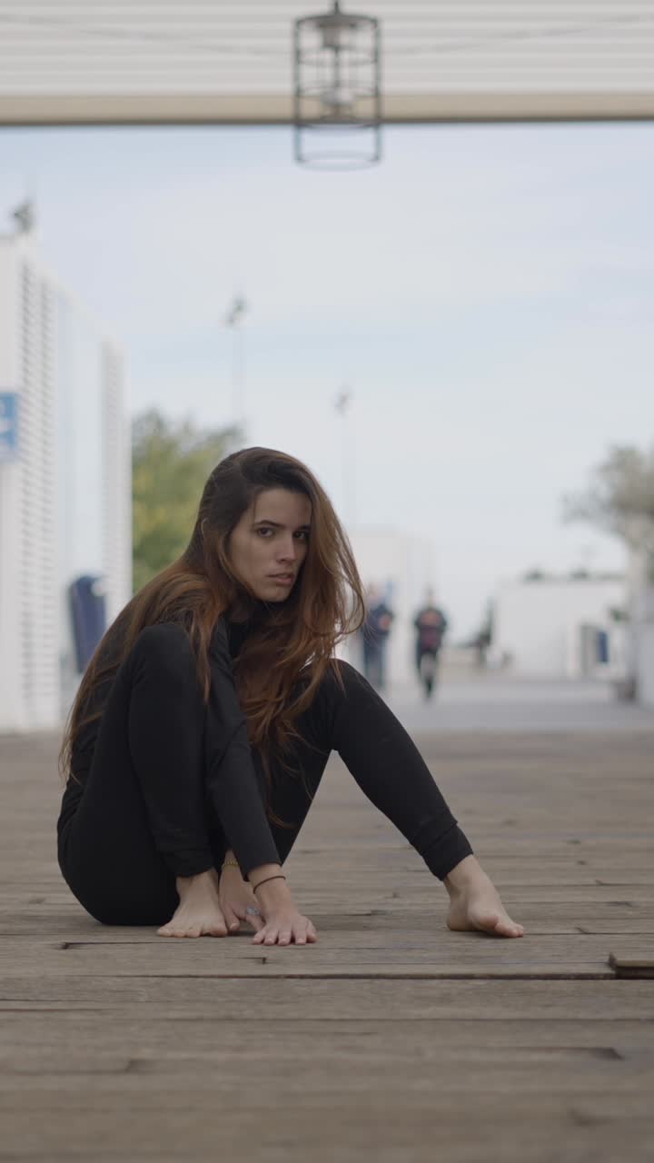 A thoughtful woman in a black outfit sits on a wooden boardwalk