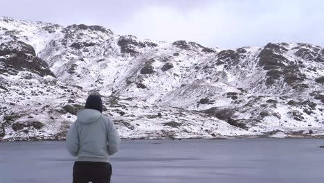 un hombre mirando una escena de montaña congelada sobre un tarn en invierno en el distrito de los lagos