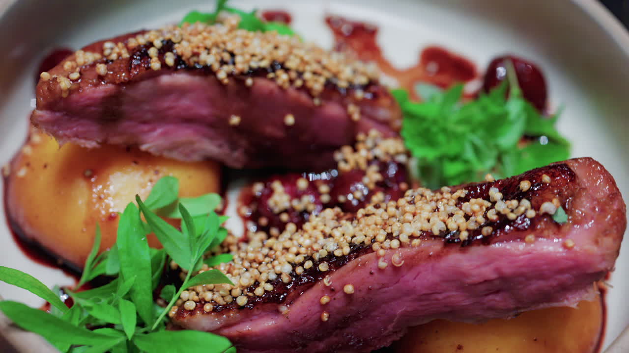 Close up of roasted duck breast plated with caramelized pear, crispy grains, and green herbs