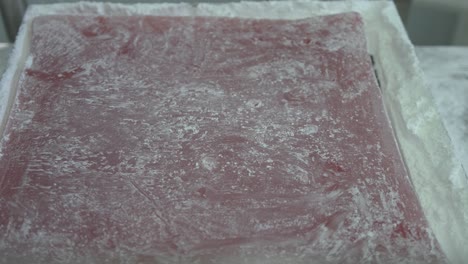 a slab of cooked turkish delight is placed down and a factory worker spread flour over the top