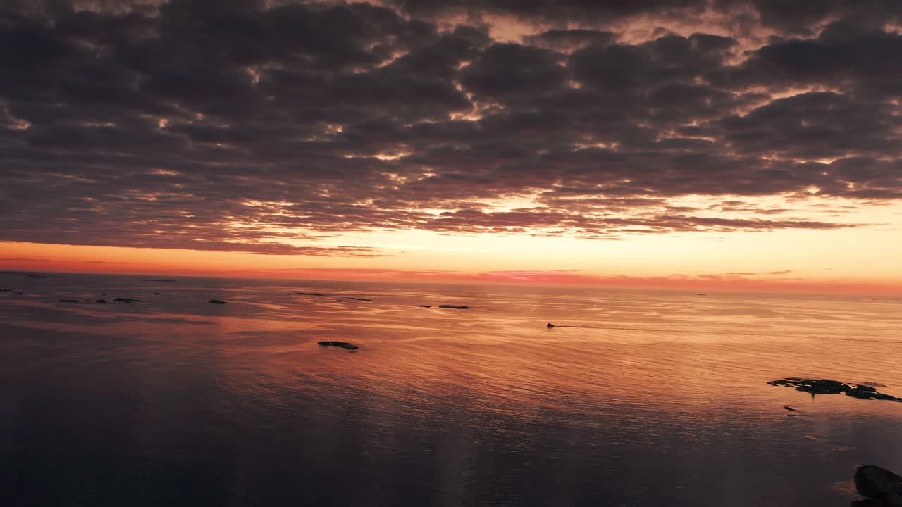 Dramatische Aufnahme von dunklen, schweren Wolken, die vom rosa-orangefarbenen Sonnenuntergang hinterleuchtet werden und sich im ruhigen Meer spiegeln