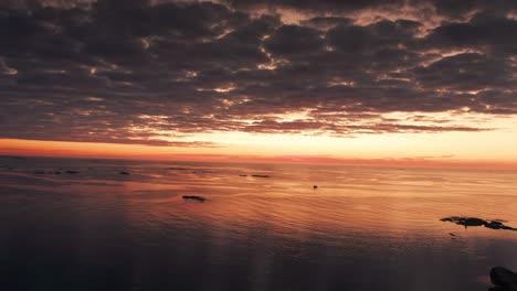 Dramatic-shot-of-the-dark-heavy-clouds-backlit-by-the-pink-orange-sunset-reflecting-in-the-calm-sea