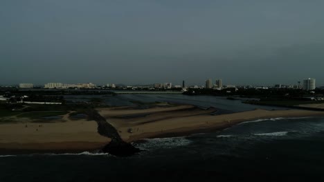 Imágenes-De-Drones-De-La-Playa-Con-Un-Remanso-Que-Se-Abre-Hacia-Ella-Con-Un-Horizonte-De-La-Ciudad-Con-Rascacielos-En-El-Fondo