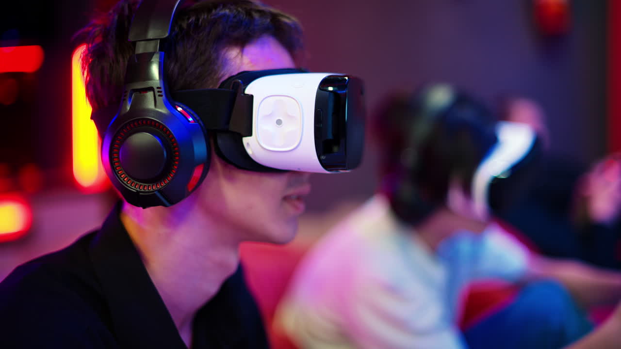 Primo piano di un adolescente che gioca a una console di gioco con visore VR e cuffie usando un gamepad. Illuminazione blu e rossa