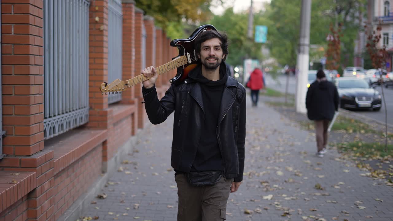 어깨에 기타를 들고 거리를 고 있는 행복한 남자