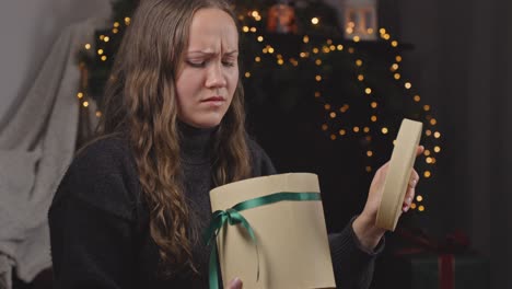 side angle view of woman receiving holiday gift in round box disappointed, hurries to hand it back