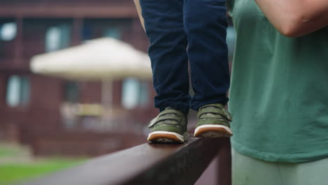 little boy walks along wooden railing with mother help