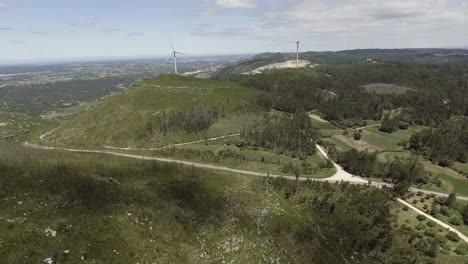 wind turbines on the lush mountains generating renewable energy in reguengo do fetal, batalha, portugal - aerial drone, pullback shot