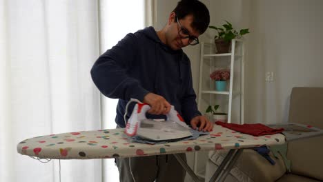 man in hoodie irons baby clothes on colorful board in cozy living room setting