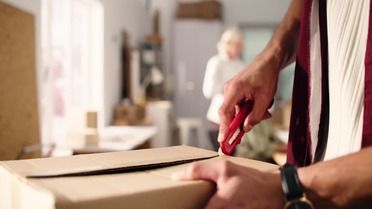 Close Up of Person's Hands Opening Cardboard Box with Utility Knife