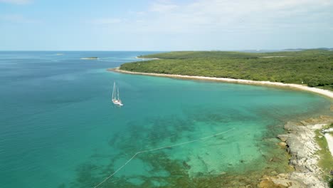 Luftaufnahmen-Eines-Weißen-Segelboots-Im-Ruhigen-Mittelmeer-Vor-Einer-Paradiesischen-Insel-Mit-Türkisblauem-Meer-Und-üppiger-Grüner-Vegetation,-Kroatien-Drohne-4k