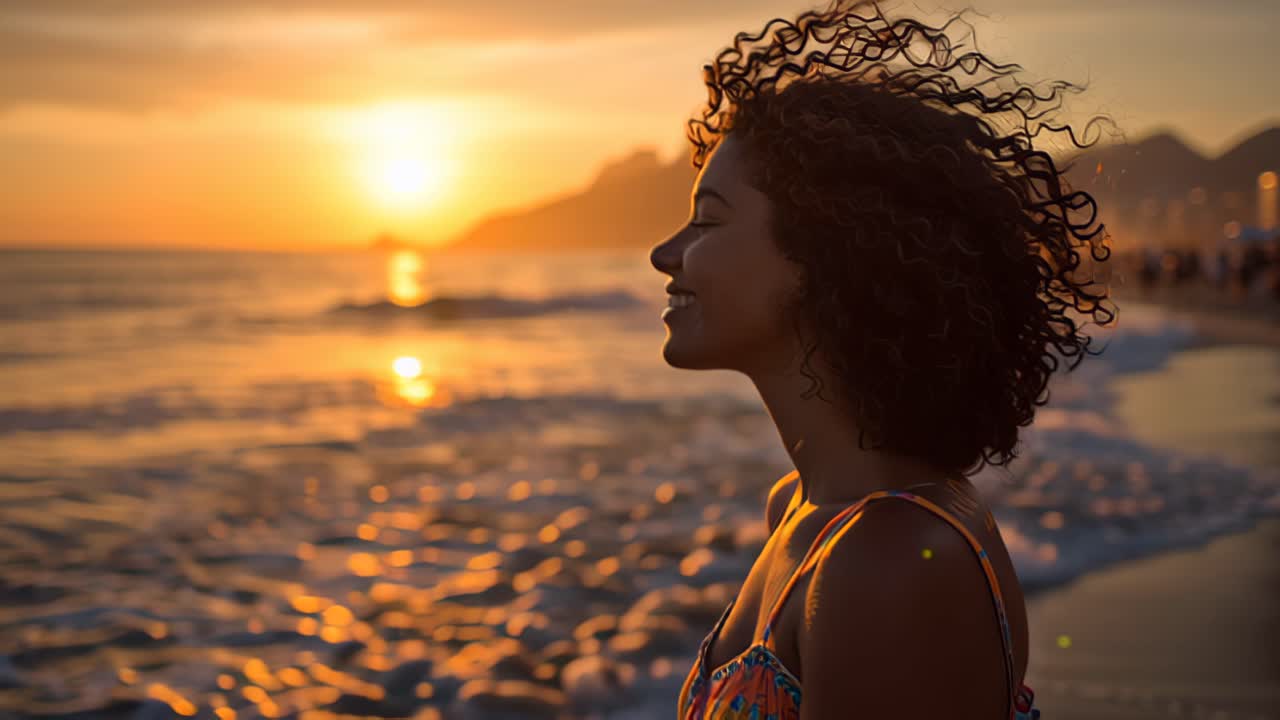 Relaxed young woman with curly hair smiling in profile as she enjoys a colorful ocean sunset, gentle waves and golden light creating a serene, carefree summer beach atmosphere