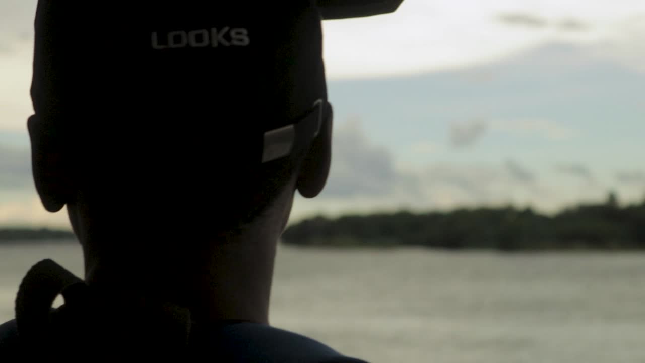 An abstract rack focus shot of a young African man looking out from the side of a boat, appreciating the mighty Zambezi river and beautiful scenic landscape surrounding the Victoria Falls, Zimbabwe