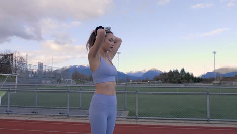 Athletic-young-woman-pulling-hair-back-into-bun-on-track-and-field