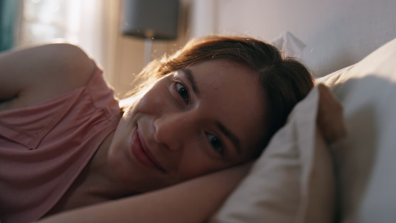mujer sonriente acostada en la cama por la mañana. mujer serena y tranquila mirando la cámara descansando