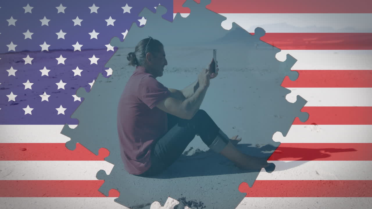 animación de rompecabezas de la bandera estadounidense que revela a un hombre usando un teléfono inteligente sentado en la playa