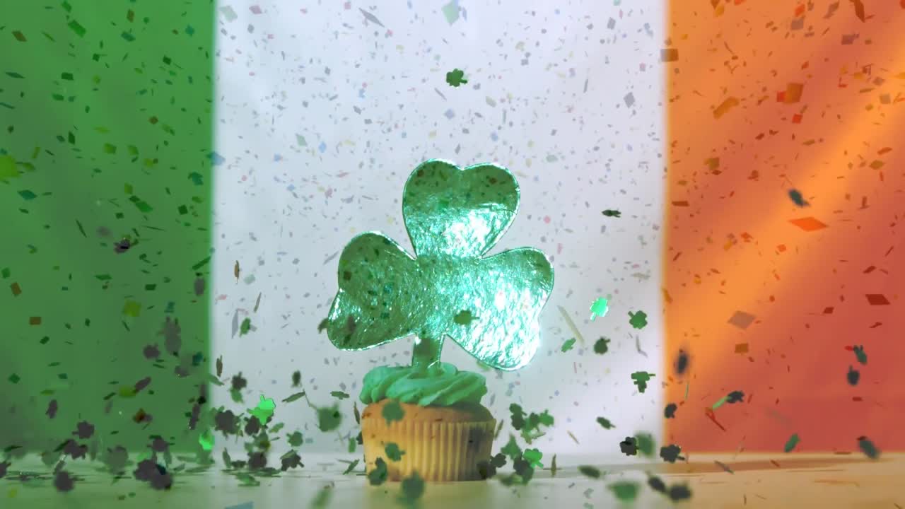 Herabfallende Papier-Kleeblätter und Cupcake mit Kleeblatt-Deko vor irischer Flagge