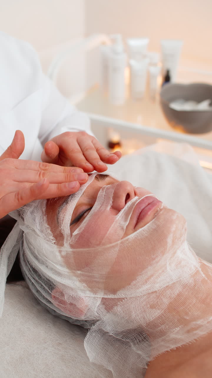 Woman receiving facial gauze wrap for carboxytherapy in cosmetology skin covered with serum moisture