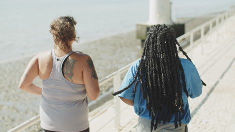 back view of multi ethnic friends running next to water