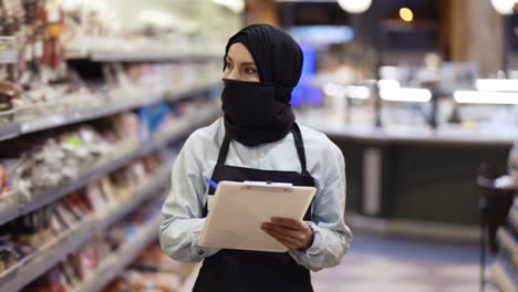 Mujer-Con-Pañuelo-Negro-Trabajando-En-La-Tienda,-Inspeccionando-Estantes-Con-Tableta,-Cámara-Lenta