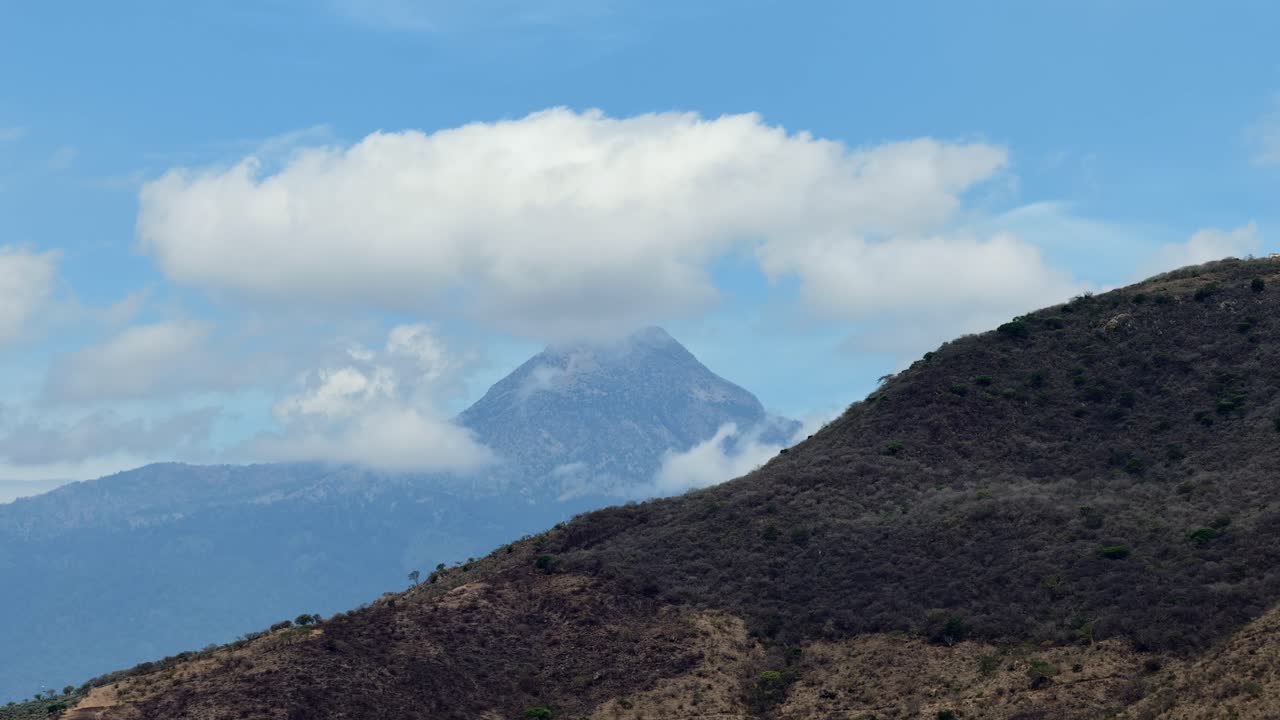 Slow motion pan left aerial overlooking Cerro Cihuapilli near Tuxpan Jalisco, reveals the Colima Volcano with sky partially covered by clouds