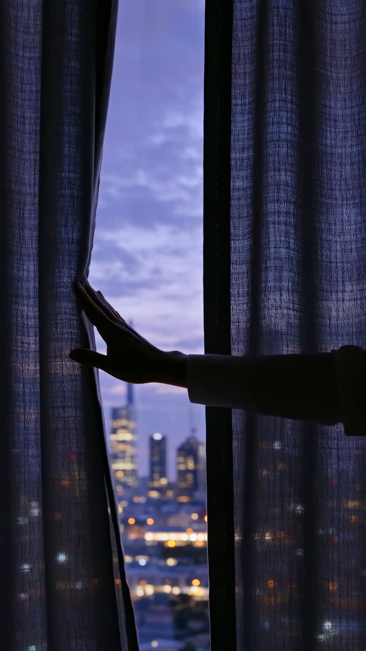 Hand opening curtain to reveal city skyline at dusk
