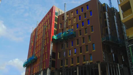 builders and construction workers using scaffold hoist lift on new colourful cladding for residential flats in london, uk