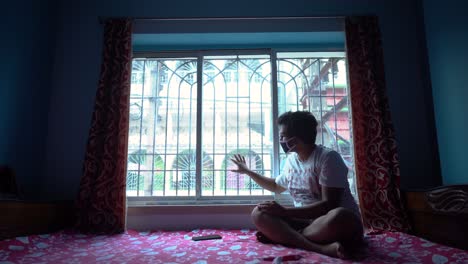 bored indian male sitting at home near window due to coronavirus quarantine, self isolation and social distancing