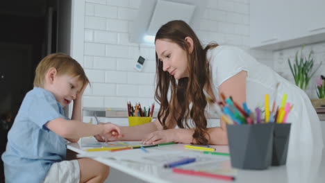 Mamá-Ayuda-A-Su-Hijo-A-Realizar-La-Tarea-Preescolar-Para-Dibujar-Un-Dibujo-A-Lápiz-Sentado-En-La-Mesa-De-La-Casa