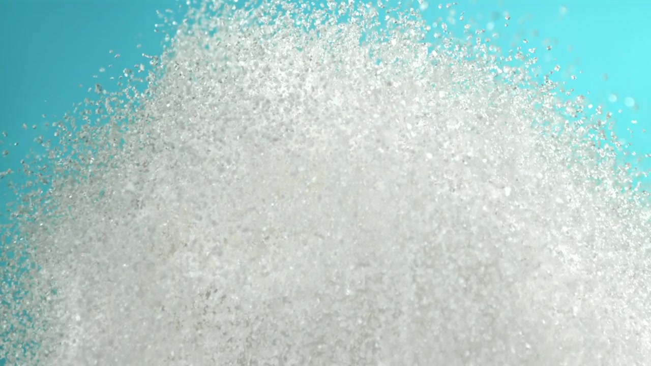 Esplosione al rallentatore di cristalli di zucchero bianco su sfondo blu.
