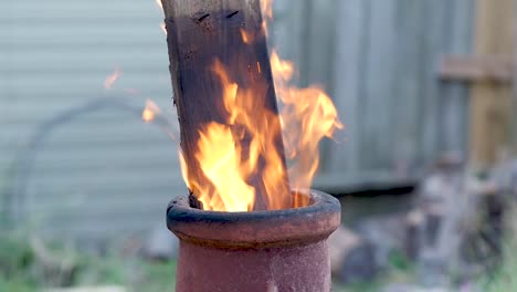 Slo-Mo:-Ein-Brett-Ragt-Aus-Der-Oberseite-Eines-Terrakotta-Kamins,-Während-Flammen-Am-Späten-Abend-Darum-Herum-Aufsteigen