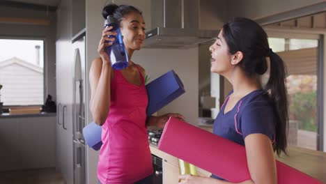 Video-of-happy-diverse-female-friends-holding-yoga-mats-and-talking-at-home