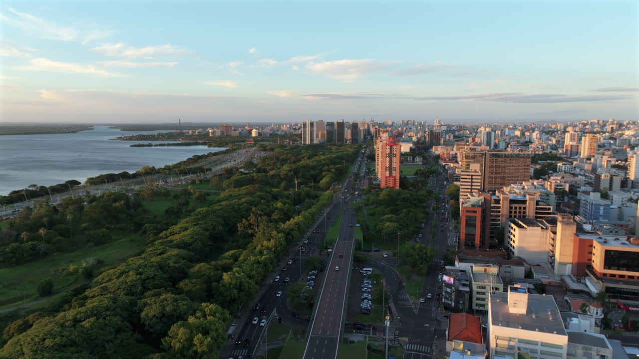 Un'ascesa verticale rivela lo skyline di Porto Alegre e il lungomare di Guaiba al tramonto sul lago Guaiba. Catturato in D-Log con colore a 10 bit.
